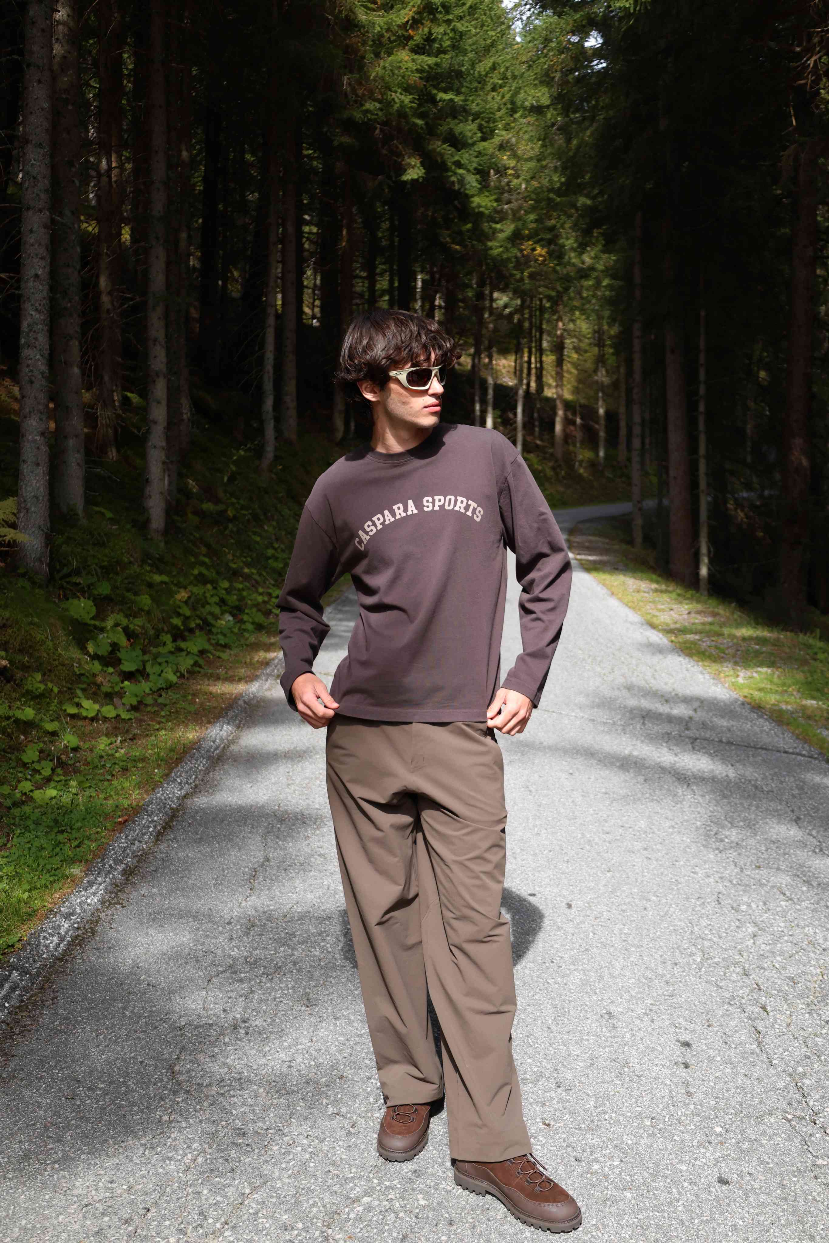 Man wearing an espresso CASPARA CS Signature long sleeve shirt standing on a forest road.